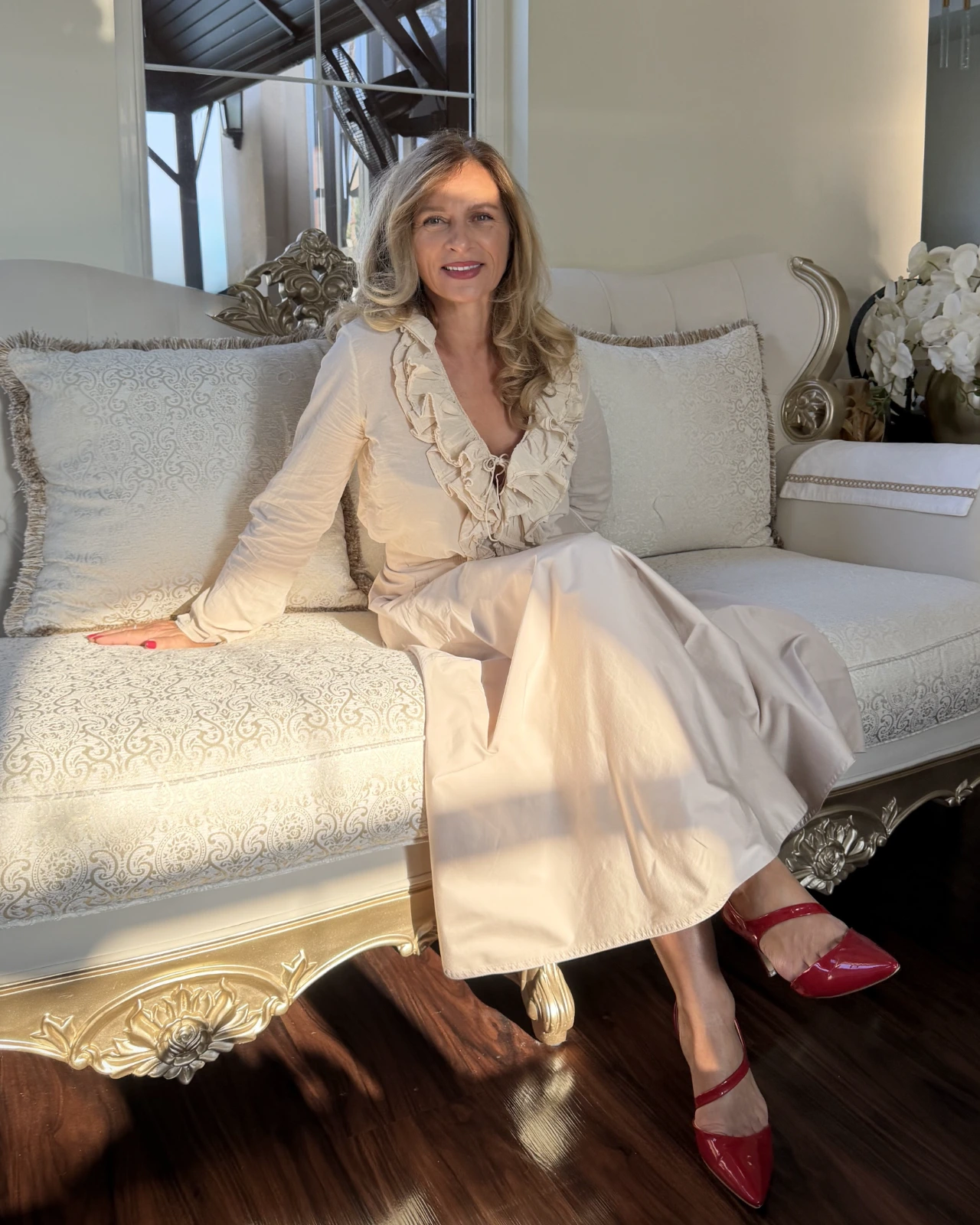 Branka, founder, seated on a cream sofa in a sunlit living room.